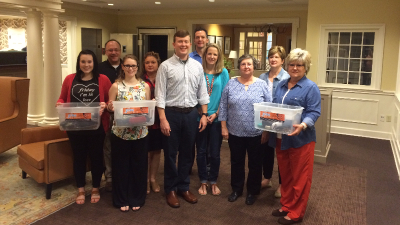 group of bank employees holding three large bins of glasses that were collected for mission trip to uganda